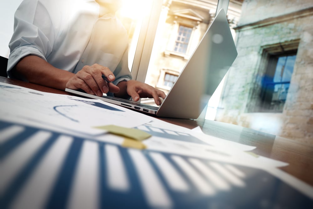 business documents on office table with smart phone and digital tablet and graph financial diagram and man working in the background